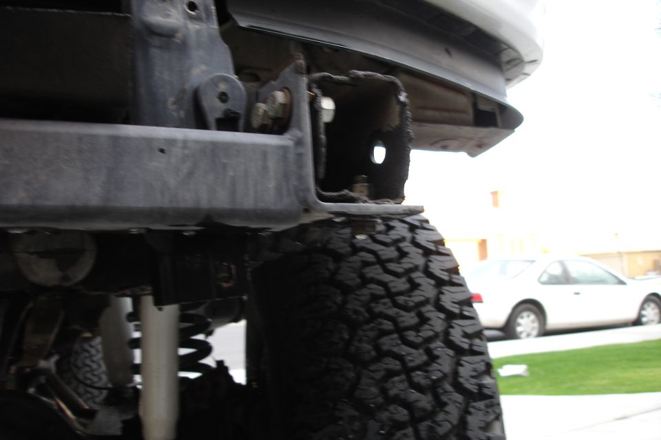 Rear bumper bracket and tire of an off-road vehicle. White car in background