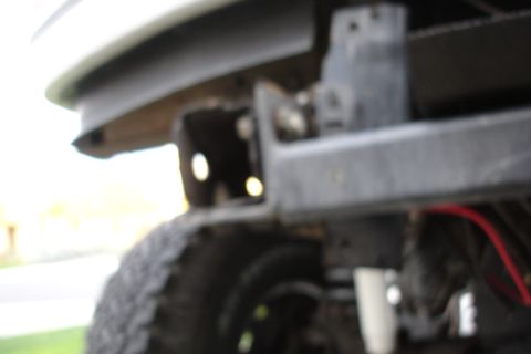1996 Ford Bronco - Detail of a vehicle's bumper mounting bracket, showing structural components and a tire.