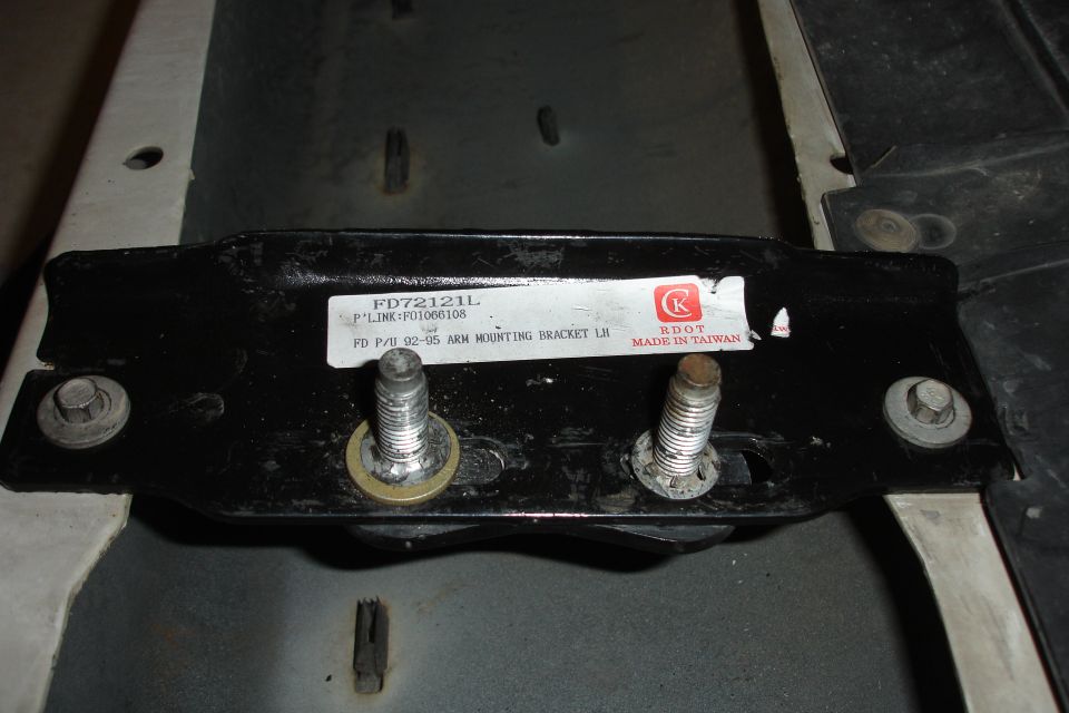 Black metal mounting bracket with two bolts and a label reading "FD P/U 92-95 ARM MOUNTING BRACKET LH"