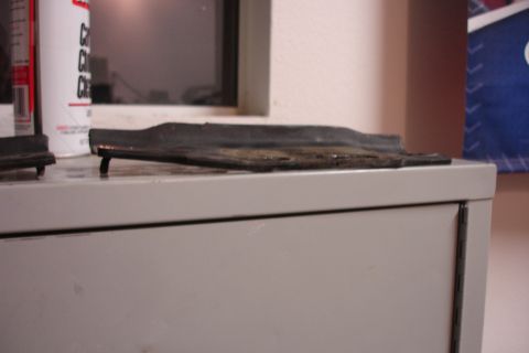 1996 Ford Bronco - A black rubber trim piece, possibly from a vehicle bumper, rests on a light gray surface next to a can.