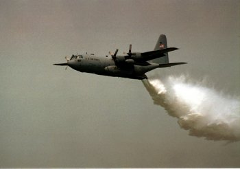 1991 Ford Probe - A Lockheed C-130 Hercules aircraft is seen in mid-flight, dispensing a stream of water.