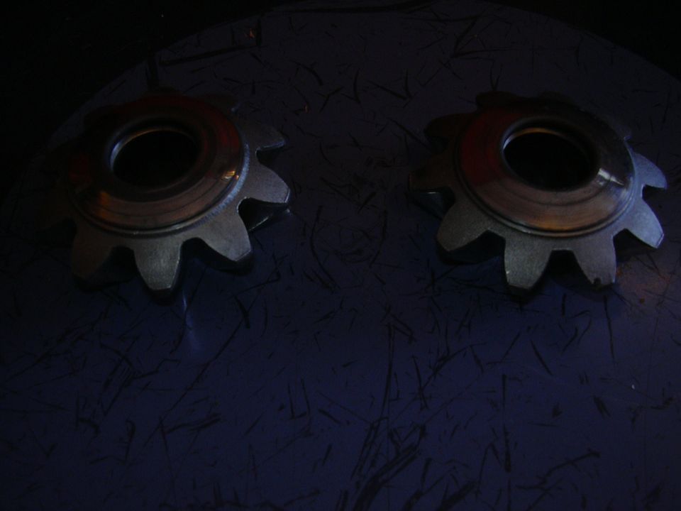 Two metal gears with ten teeth each, resting on a dark textured surface