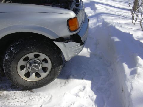 1996 Ford Crown Victoria - Front corner of a silver SUV with a damaged bumper sits in deep snow, hood up.