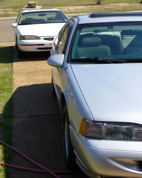 1995 Ford Thunderbird - A silver 1995 Ford Thunderbird is parked in front of a white one, showing the front quarter of the silver car.