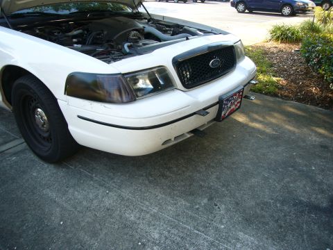 2000 Ford Crown Victoria - A white Ford Crown Victoria is shown from the front with its hood up, revealing the engine compartment and a black grille.