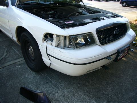2000 Ford Crown Victoria - A white Ford Crown Victoria is parked outside with its hood up and the driver's side headlight removed.