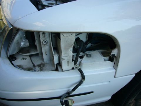 2000 Ford Crown Victoria - Close-up view of a white car's front headlight assembly, showing exposed wiring and mounting points.