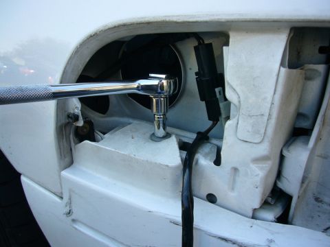 2000 Ford Crown Victoria - A close-up view shows a ratchet wrench being used to secure a component on the exterior of a white vehicle.
