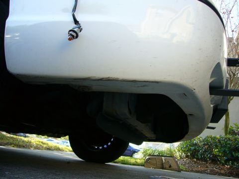 2000 Ford Crown Victoria - The front bumper of a white 2000 Ford Crown Victoria is visible from a low angle, with the undercarriage and a loose headlight on the groun…