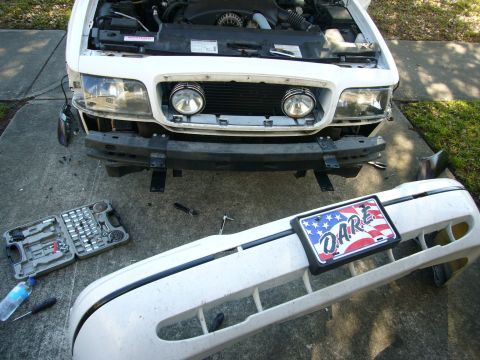 2000 Ford Crown Victoria - White sedan on a driveway with the hood up and the front bumper cover removed and laid on the concrete in the foreground, still wearing its…