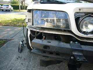 2000 Ford Crown Victoria - Front view of a white car, missing a headlight and with a push bumper installed. A second vehicle is visible in the background.