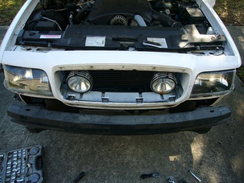 2000 Ford Crown Victoria - The front of a 2000 Ford Crown Victoria is shown with the hood up and bumper removed, revealing the engine and grille area.