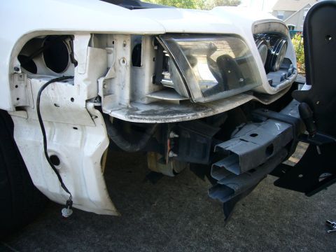 2000 Ford Crown Victoria - Front-end disassembly on a white sedan with the bumper cover and grille removed, exposing the radiator support, headlight buckets and a dan…