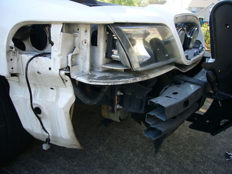 White sedan front end stripped down, bumper cover off, headlight and radiator support exposed