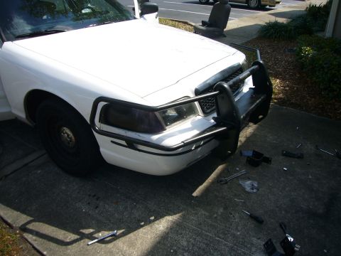 2000 Ford Crown Victoria - Front view of a white 2000 Ford Crown Victoria, possibly a police vehicle, with a push bumper installed and tools scattered nearby.