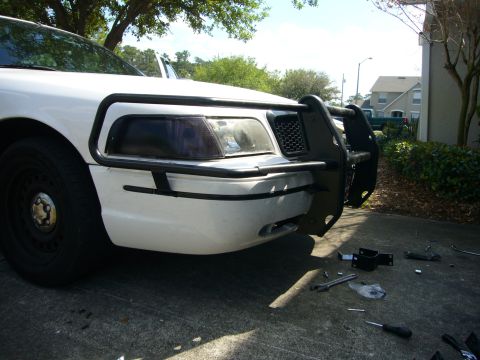 2000 Ford Crown Victoria - Front view of a white 2000 Ford Crown Victoria fitted with a Go Rhino push bumper, with installation hardware on the ground.
