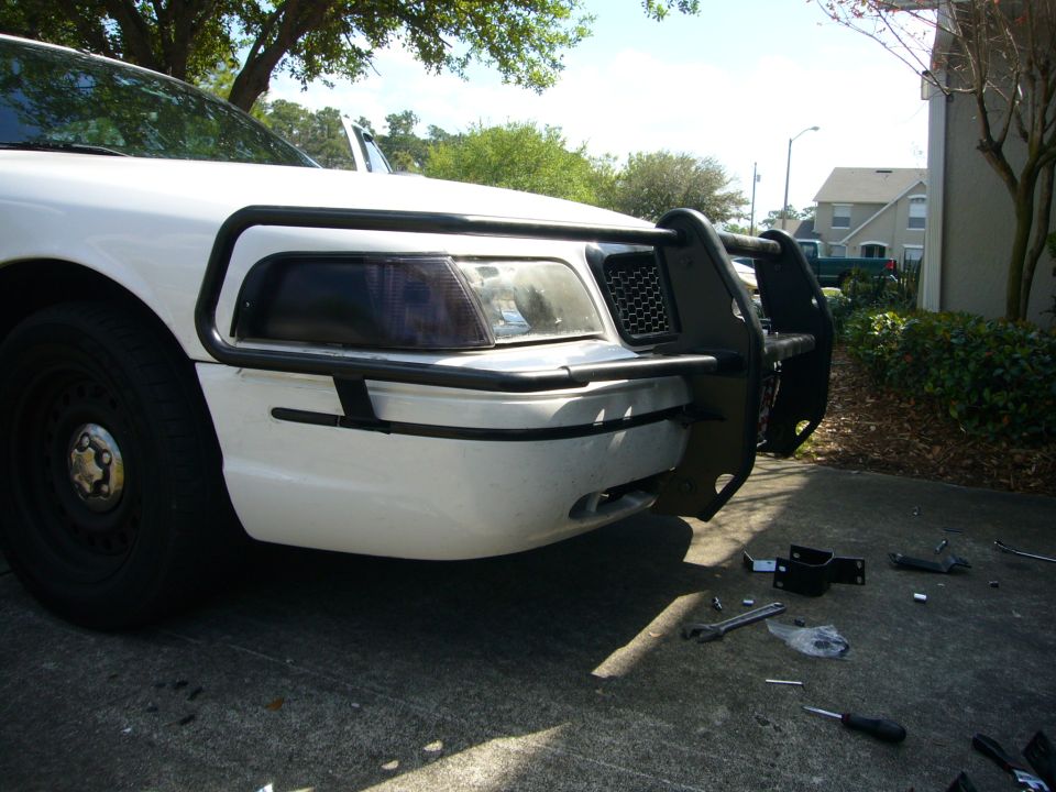 White 2000 Ford Crown Victoria front end with black push bumper installed, tools scattered on pavement