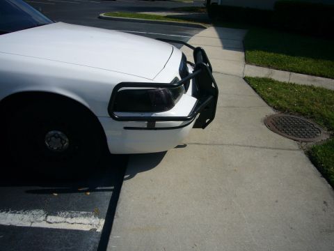 2000 Ford Crown Victoria - Three-quarter front view of the driver's side of a white Ford sedan parked at a curb, showing a black tubular push bar with headlight guard…