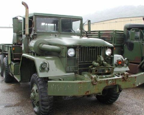 1985 Ford Bronco - A military truck with a tall exhaust pipe is parked next to another similar vehicle.