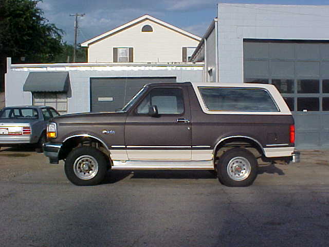 Side view of a two-tone brown and white Ford Bronco SUV parked in front of buildings