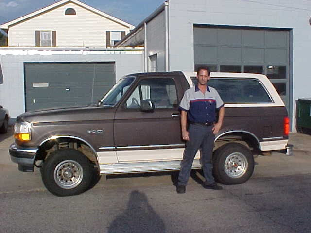 Two-tone brown and white Ford Bronco SUV, side view, with a man standing beside it in front of a garage