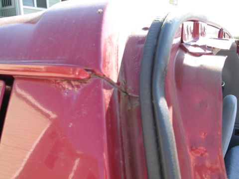 1995 Ford Bronco - Close-up of a red vehicle's door frame showing rust and a rubber seal.