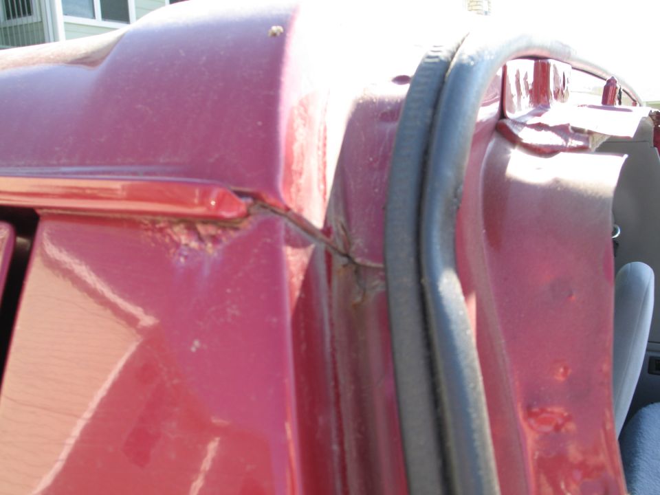 Red vehicle door frame with visible rust and a rubber seal. Close-up view