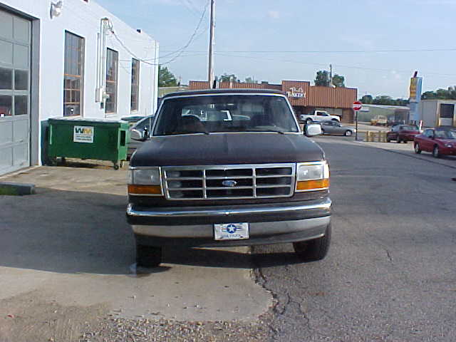 Front of black 1990s Ford F-series truck with chrome grille at a shop lot