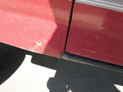 1995 Ford Bronco - The lower section of a red vehicle's doors shows a small rust spot near the seam.