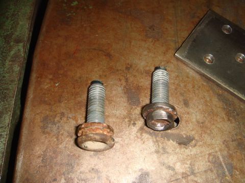 1996 Ford Bronco - Close-up view of two corroded bolts and a metal plate on a workbench.