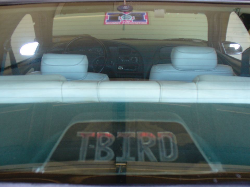 Interior view of a car's rear seats and dashboard, with 'TBIRD' emblem on the rear window