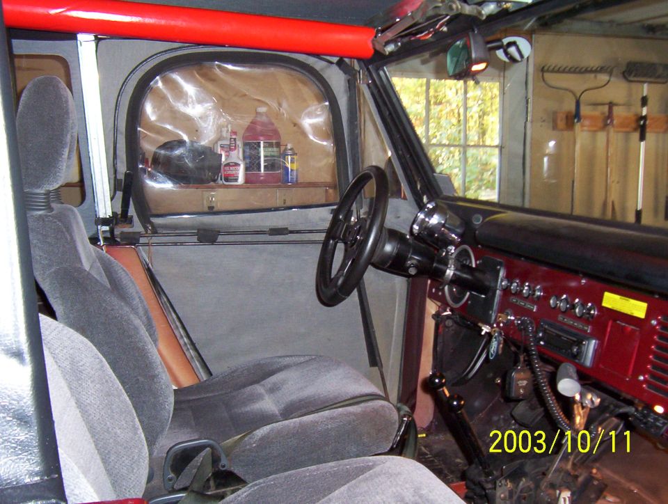 SUV interior with gray cloth buckets, maroon dash with toggle switches, red padded roll bar, and soft top windows