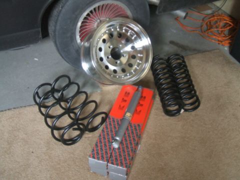 1974 Ford Ranchero - A collection of automotive suspension components, including new shocks and springs, are laid out next to a car wheel.