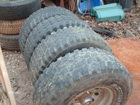 1990 Ford F-150 - A stack of four off-road tires sits on the ground next to some debris.