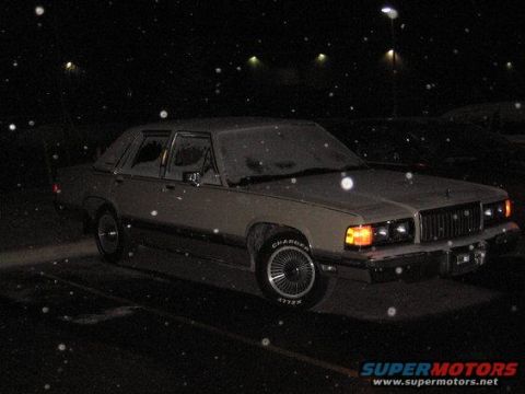 1988 Mercury Grand Marquis - A tan 1988 Mercury Grand Marquis sedan is parked outside at night, with snow falling.