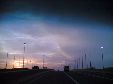 1999 Mercury Grand Marquis - Several vehicles travel along a highway as the sun sets, casting a colorful glow across the sky.