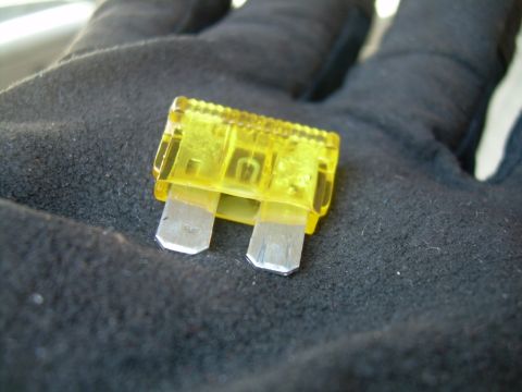 1988 Ford Bronco - A yellow automotive fuse is shown, held in a gloved hand against a dark, textured background.