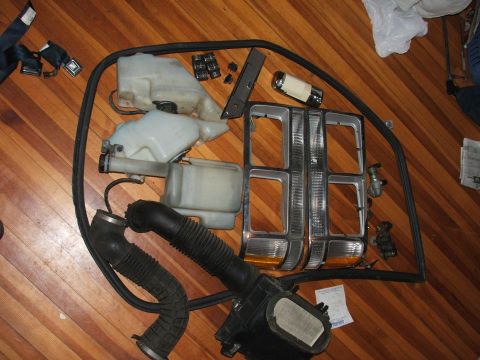 1991 Ford LTD Crown Victoria - Various car parts, including headlights and fluid reservoirs, are laid out on a wooden floor.