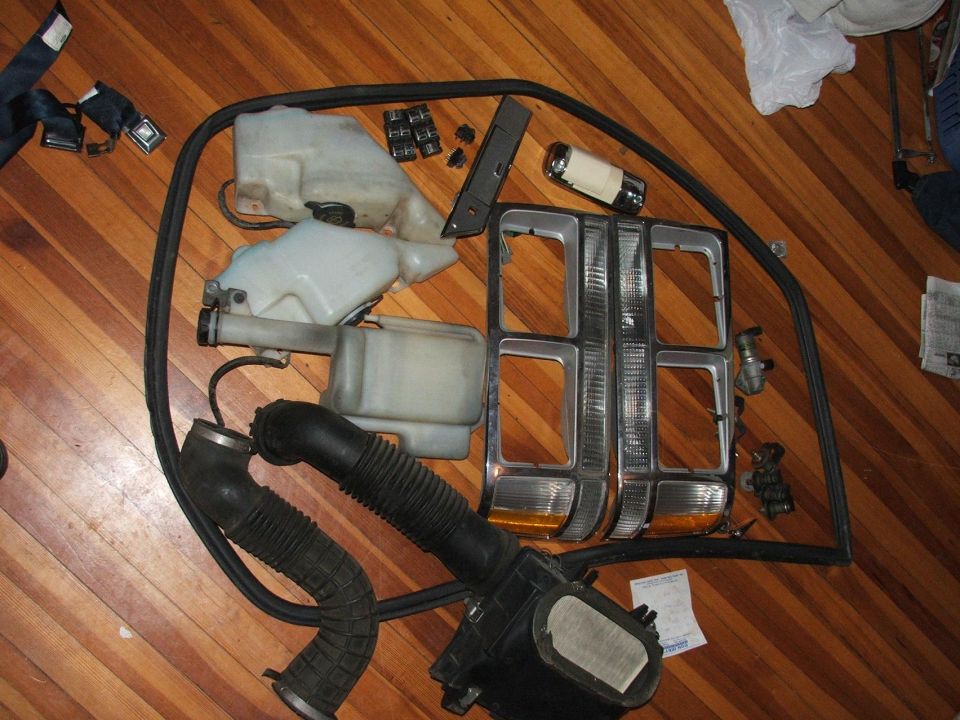 Car parts including headlights, air intake, and fluid reservoirs on a wooden floor