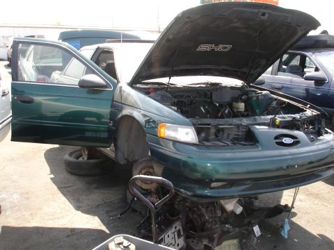 1993 Ford Taurus - Junkyard Ford Taurus SHO, front view, driver door open, engine exposed. Another vehicle is parked behind.
