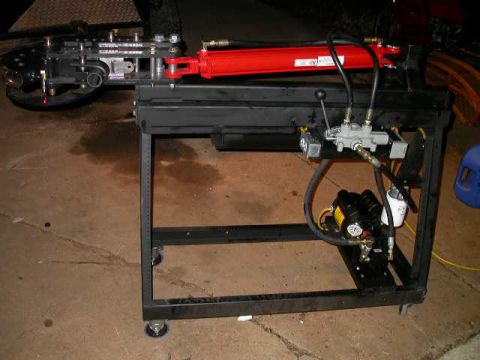 1990 Ford Bronco - A hydraulic tube bender is shown with its red cylinder and black frame, mounted on a wheeled cart.