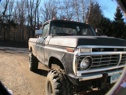 1977 Ford F-250 - A lifted Ford pickup truck is parked on a dirt road with trees in the background.