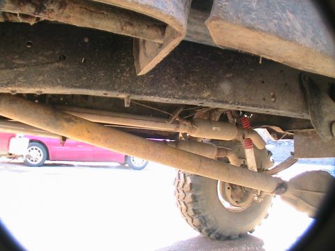 1977 Ford F-250 - The underside of a truck is shown, with a pink car visible in the background. The Supermotors.net logo is present in the lower right corner.