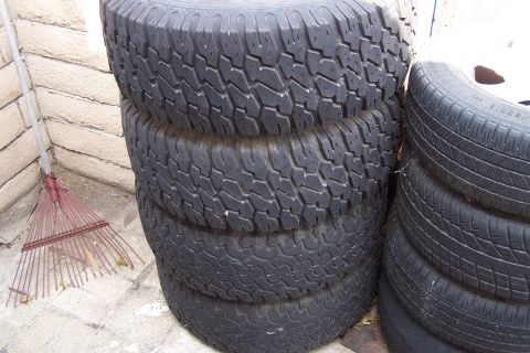 1990 Ford Bronco - A collection of used tires are stacked up outdoors next to a brick wall and a garden rake.