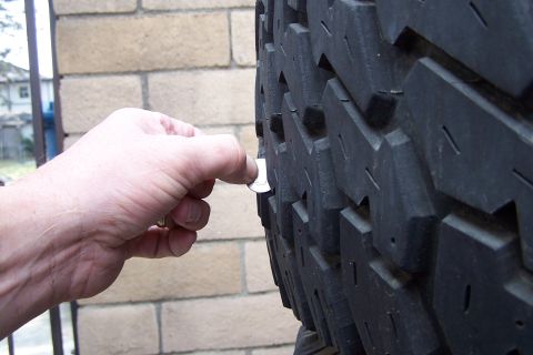 1990 Ford Bronco - A hand uses a coin to measure the tread depth of a tire.