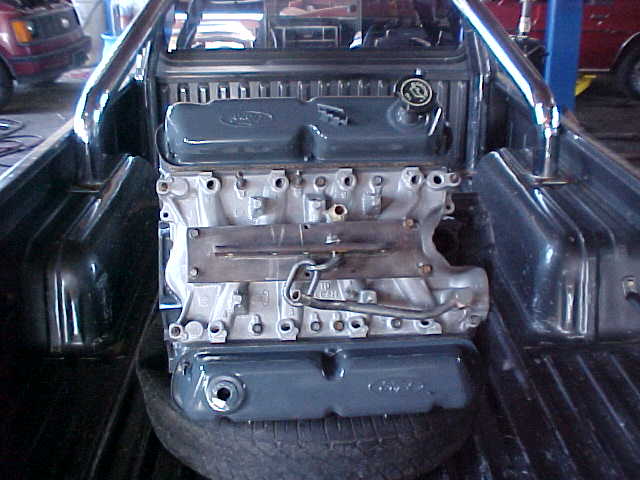Gray Ford inline engine resting on a tire in a truck bed