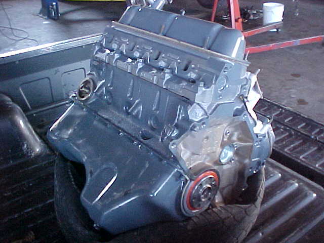 Gray painted V8 short block with heads installed sitting on a tire in a truck bed