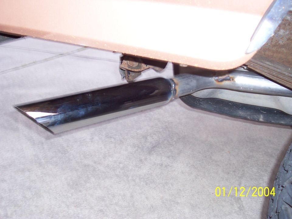 Chrome exhaust tip angled downwards, attached to a tan vehicle body. Welds visible on exhaust pipe