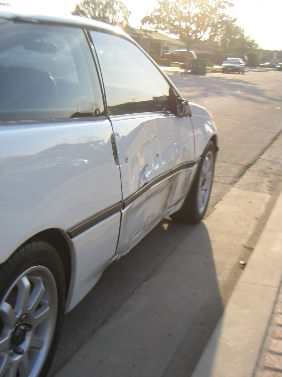 Rear quarter crash damage on a white coupe at a curb