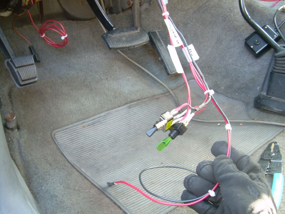 Close-up of vehicle interior showing aftermarket wiring, switches, and pedals